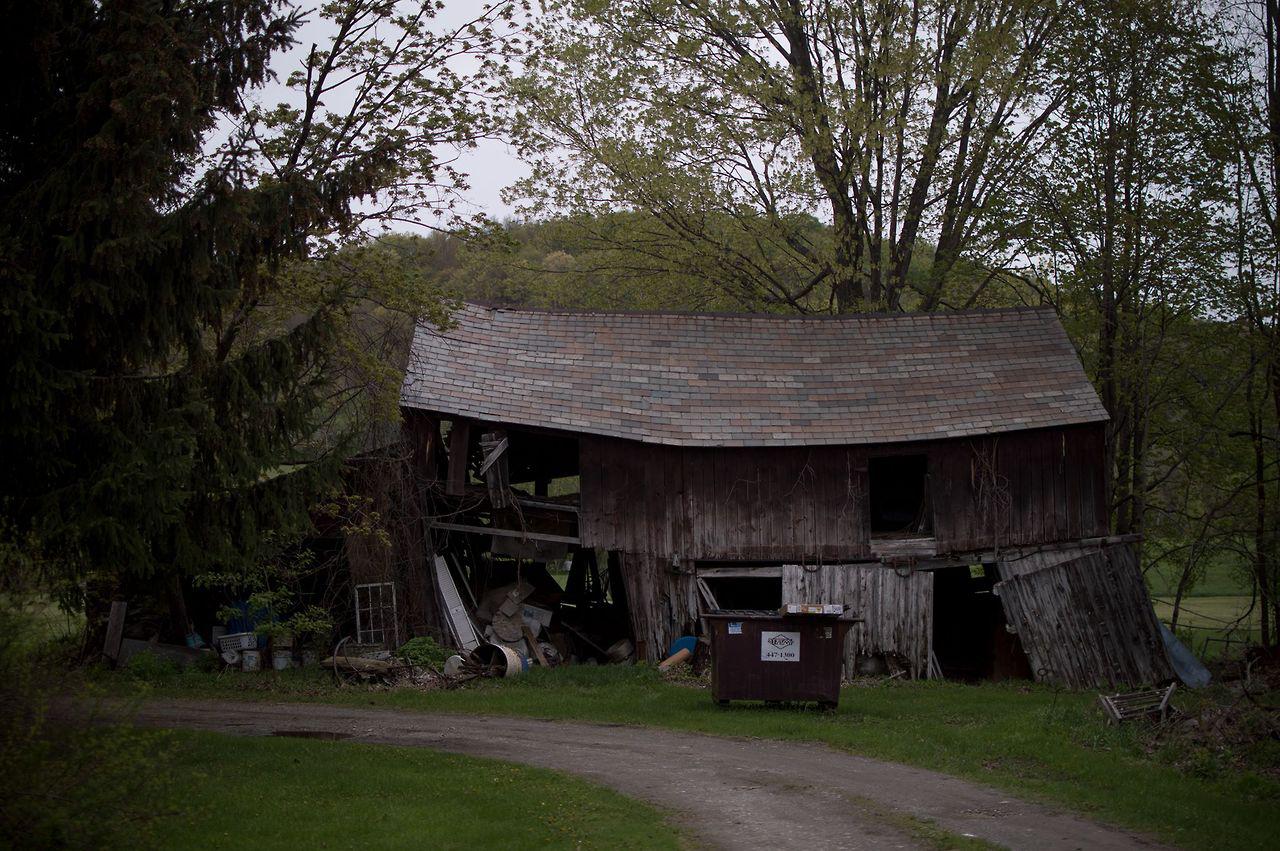 Sodom, Vermont (2017). A swaybacked barn with large sections of its front wall shattered and missing. A dumpster sits out front.