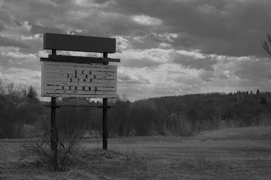Bill Laston Memorial Park, Lanesborough, Massachusetts (2017). An marquee-style sign sits in an empty field bounded by woods. The weatherbeaten letters have been arranged to read, '5 2 4 JAKE STAY STRONG.'